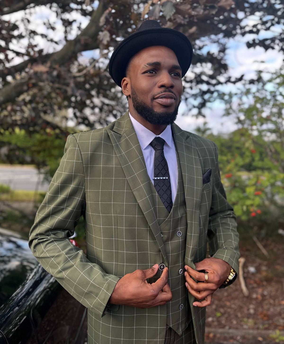 Valentine Grey in an olive windowpane three-piece suit and black fedora.